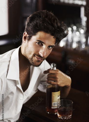 Man, pub counter and portrait with drink at happy hour with alcohol and whiskey after work. Bottle, male person and face of a handsome guy with a glass and style and confidence in a luxury bar