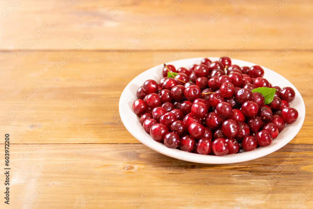 ripe red cherries in a white plate on a wooden background. Rich harvest in the garden. Fresh and healthy organic food ripe red cherries in a white plate on a wooden background. Rich harvest in the garden. Fresh and healthy organic food