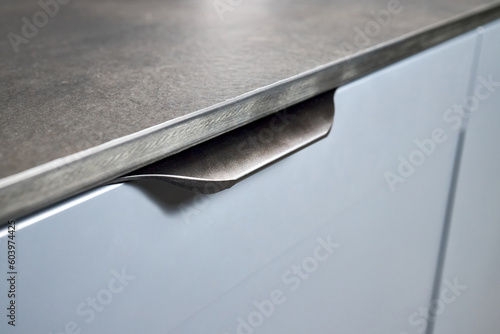 Pull out rack cabinet drawer handle closeup. Flush up slip handle finger pull profile handle of contemporary kitchen drawer with grey blue facade and compact high pressure laminate HPL countertop. photo