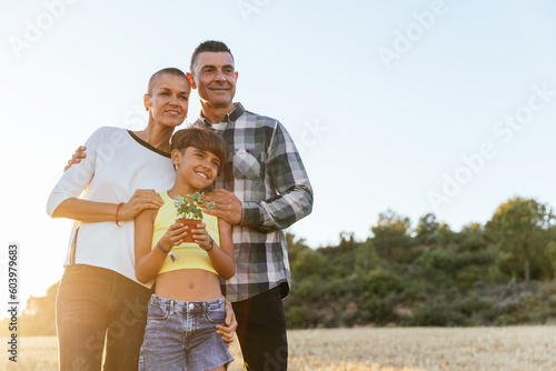 Happy family smiling while posing together outdoors in the field with a plant.