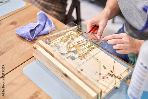 Master class on creating frame with Herbarium in tiffany technique in stained glass. A woman lays out a composition. Herbarium of dried different plants and flowers placed under a glass