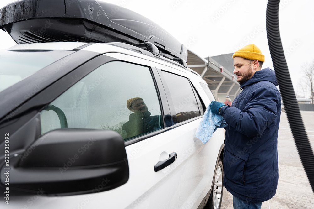 Man wipes american SUV car with a microfiber cloth after washing in cold weather. Man wipes american SUV car with a microfiber cloth after washing in cold weather.