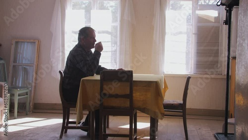 Retired elderly man, sitting alone sipping coffee at rustic table. Side profile