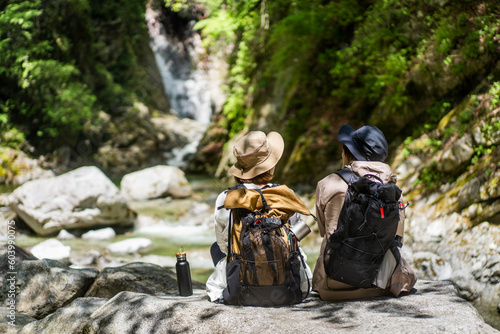 Foto 岩に座り滝を眺めながら休憩をしている登山者２人/
トレッキング