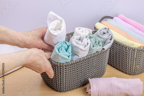 Women's hands fold clean clothes. Vertical storage of clothing in the baskets. Closet cleaning