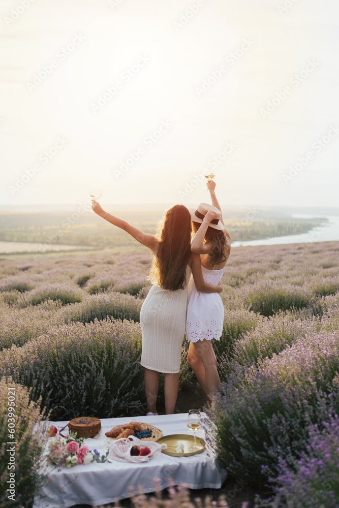 Back view of two female friends walking outdoors at the lavender field. They enjoying fresh air, beautiful nature.