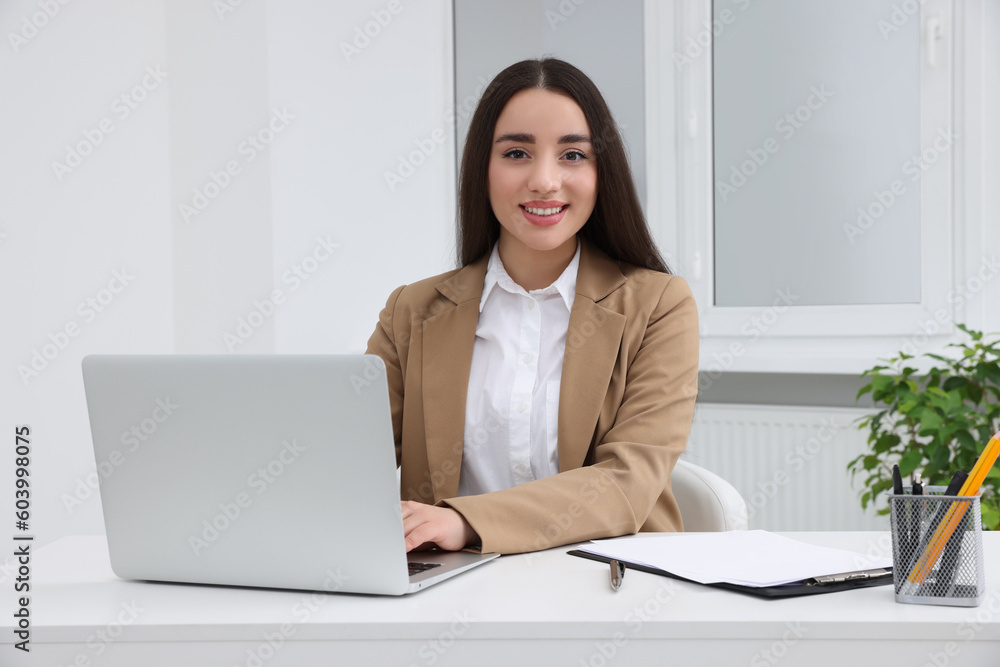 Young female intern working with laptop at table in office Young female intern working with laptop at table in office