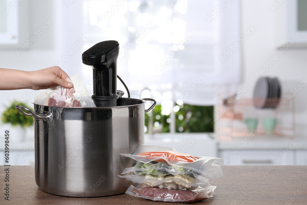 Woman putting vacuum packed meat into pot with sous vide cooker on wooden table in kitchen, closeup. Thermal immersion circulator - obrazy, fototapety, plakaty 