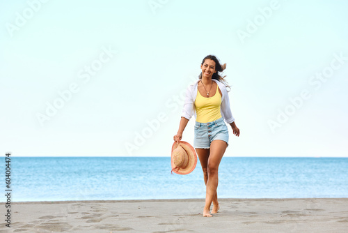 Happy woman walks barefoot on sand while spending summer day on beach.