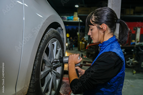Young female mechanic checking the air pressure of a car's tires. © Agustin