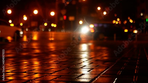 Glowing circles from street lighting are blurred. The headlights of cars passing by are reflected on the surface of the tile.