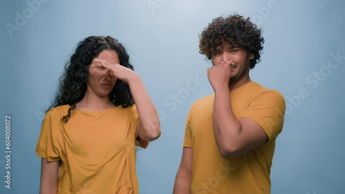 Bad smell reaction multiracial diverse couple Indian Arabian man and Hispanic woman cover noses suffer disgust stink stinky smelly aroma frowning sniffing unpleasant odor at blue studio background