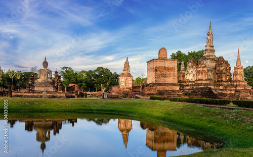 Beautiful wide view of ruins of  Wat Mahathat Sukhothai at sun set with white clouds and blue sky on background. UNESCO and World Heritage Site. Travel  Concept.