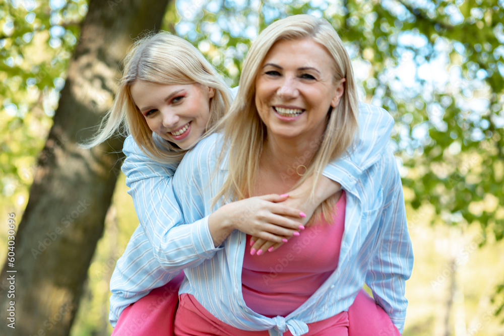 Mother and daughter, dressed in same clothes, hiking outside. Mum carry young lady on back. Happy family. Mother and daughter, dressed in same clothes, hiking outside. Mum carry young lady on back. Happy family.