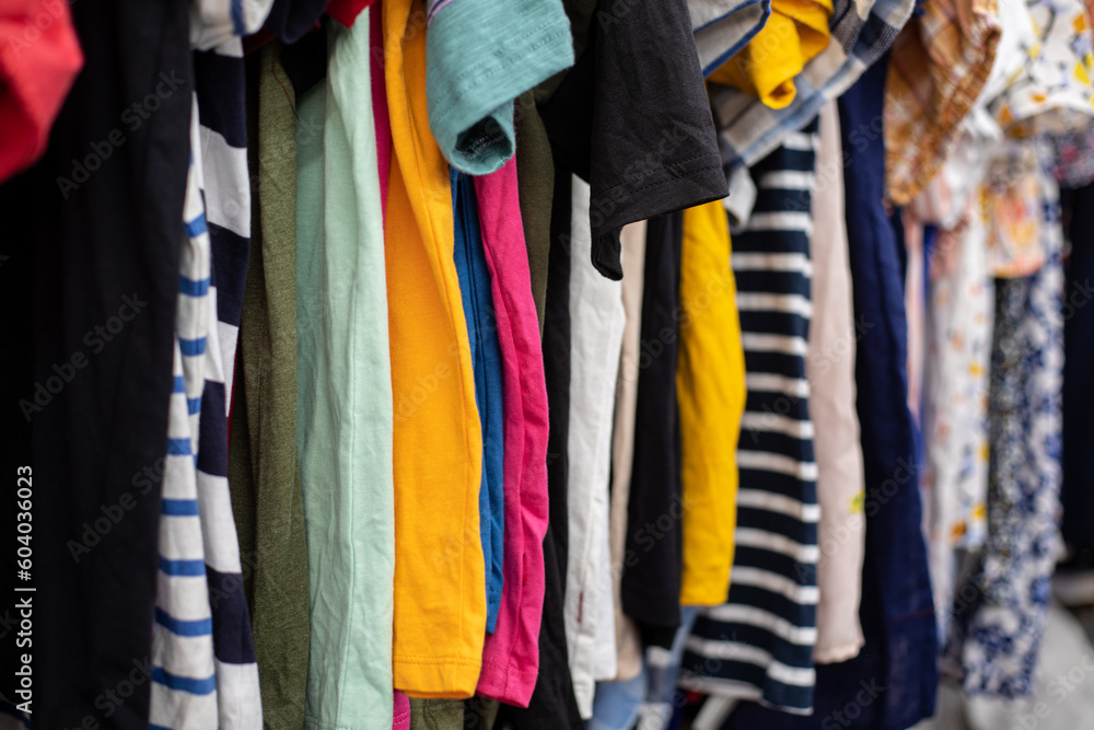 Summer T-shirts, blouses of different colors and sizes hang on hangers in discount store. Bright clothes. Outlet.