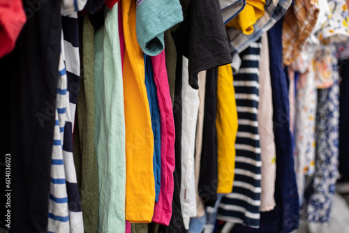 Summer T-shirts, blouses of different colors and sizes hang on hangers in discount store. Bright clothes. Outlet.