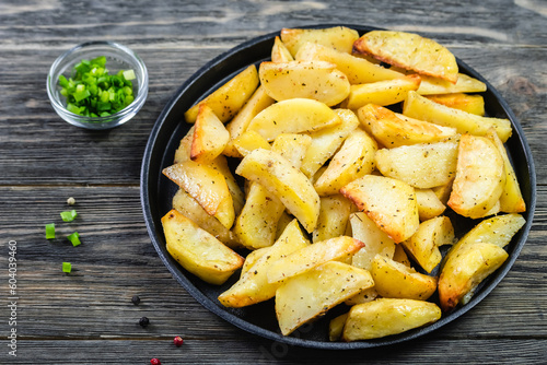 Crispy parmesan rosemary potato wedges in cast iron skillet on wooden background. Top view, copy space, flat lay.