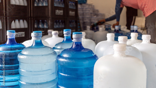 Plastic big bottles or white and blue gallons of purified drinking water inside the production line to prepare for sale. Water drink factory, small business