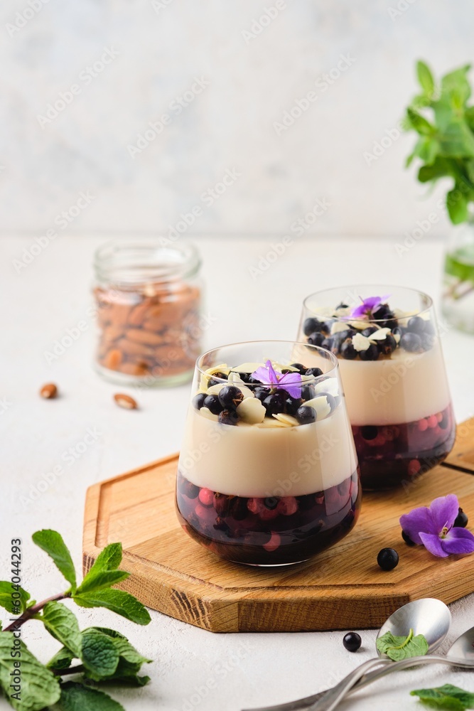 Two-layer jelly with a berry layer and a layer of almond milk panna cotta in transparent glasses on a wooden board on a light concrete background. Vegan, desserts without baking. Desserts in a glass.