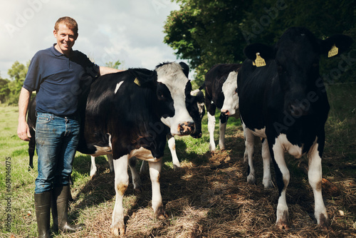 Portrait, agriculture and cows with a man on a farm outdoor for beef or natural sustainability. Confident, milk or dairy farming and a young male farmer standing on a field or meadow with animals
