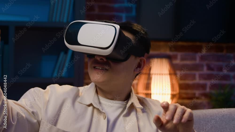 Asian man play video game virtual reality experience cyberspace world modern technology explore 3d goggles eyeglasses at night home Korean male in VR glasses helmet play simulation at evening at couch Asian man play video game virtual reality experience cyberspace world modern technology explore 3d goggles eyeglasses at night home Korean male in VR glasses helmet play simulation at evening at couch