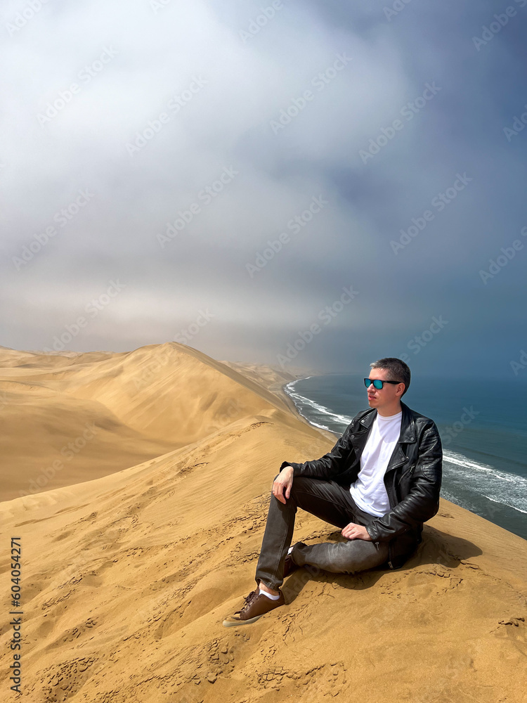 A young man sitting at sandy dunes on the seashore. Sandwich Harbour in Namibia