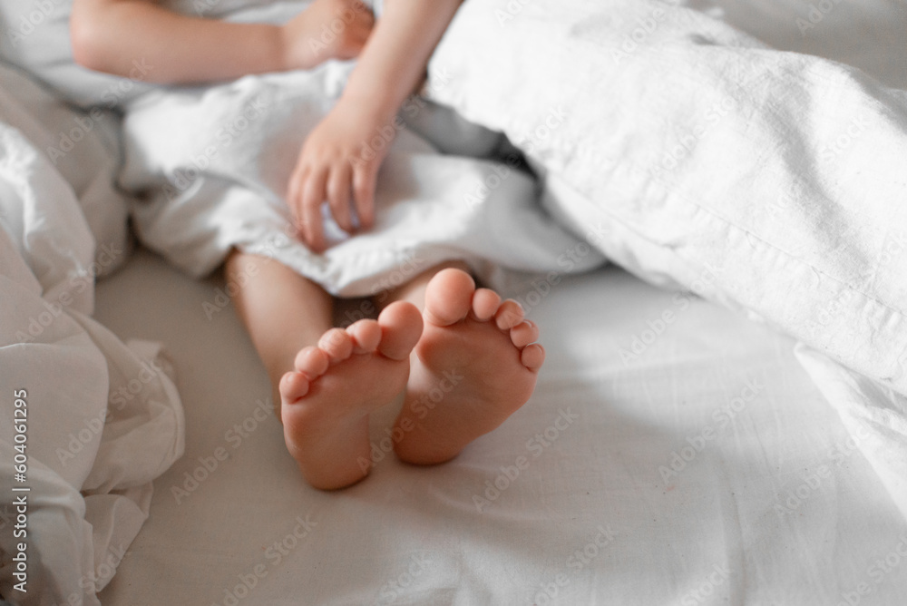 Baby feet under white cotton bed linen. Morning natural light.