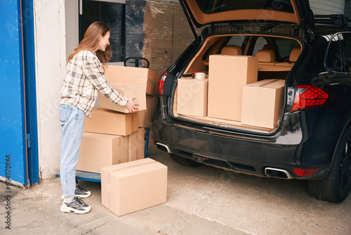 Young woman with cardboard boxes near the trunk of the car in a warehouse