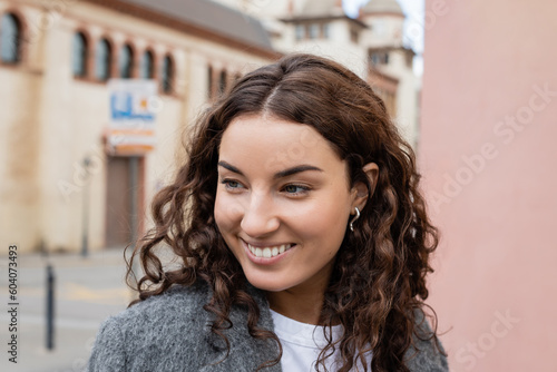 Photography Portrait of smiling and curly woman in stylish casual jacket looking away while