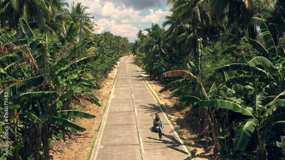 Couple, motorcycle and travel on road trip in a tropical island on street path between palm trees in nature. Man and woman traveling down route on motorbike in adventure, vacation or holiday together Couple, motorcycle and travel on road trip in a tropical island on street path between palm trees in nature. Man and woman traveling down route on motorbike in adventure, vacation or holiday together