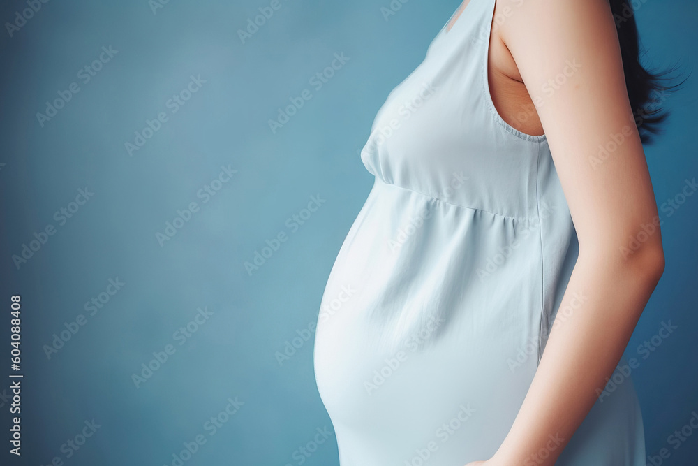 A pregnant caucasian woman in blue dress strokes her belly on blue background. Place for text. Copy space. Waiting for the birth of a child. High quality photo - obrazy, fototapety, plakaty 