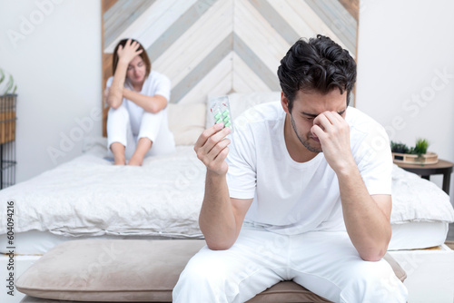 Bild auf Leinwand Frustrated and depressed man sitting on the edge of the bed and holding tablets