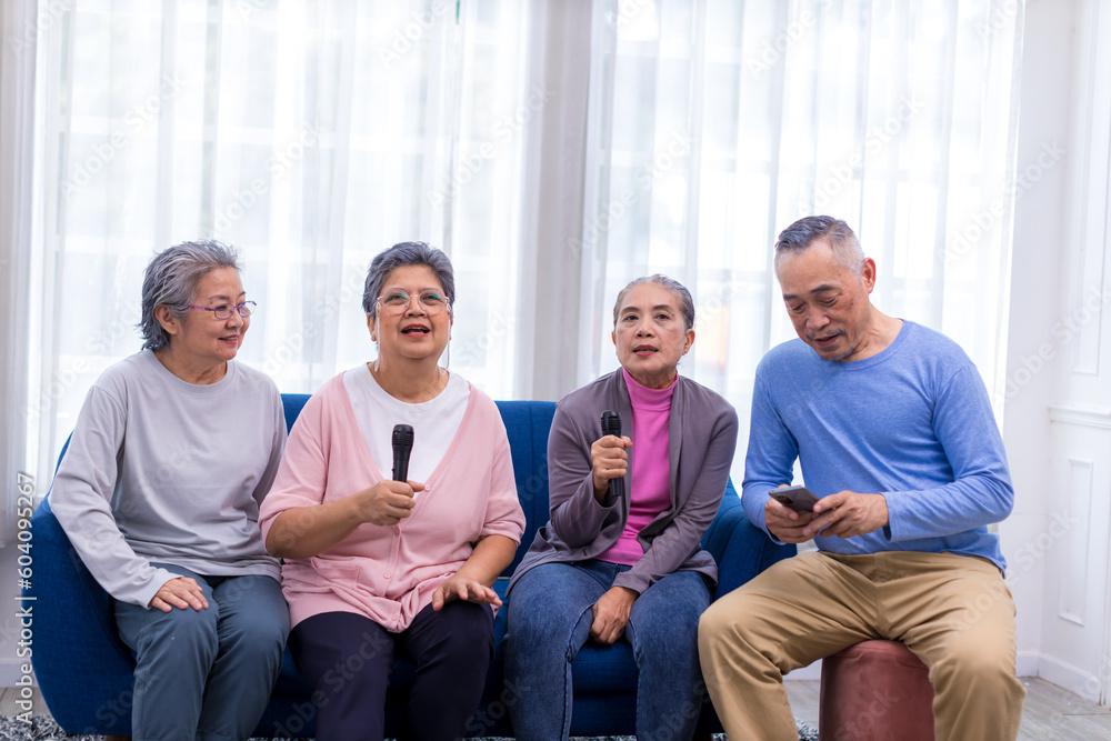 Happy senior Asian friends singing karaoke on the sofa in the living room with happy smiling face. Elderly people singing karaoke. Friends singing karaoke at home Happy senior Asian friends singing karaoke on the sofa in the living room with happy smiling face. Elderly people singing karaoke. Friends singing karaoke at home