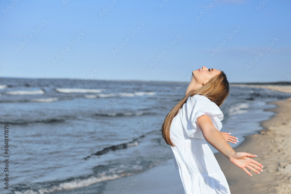 Happy, beautiful woman on the ocean beach standing in a white summer dress, open arms. Happy, beautiful woman on the ocean beach standing in a white summer dress, open arms.
