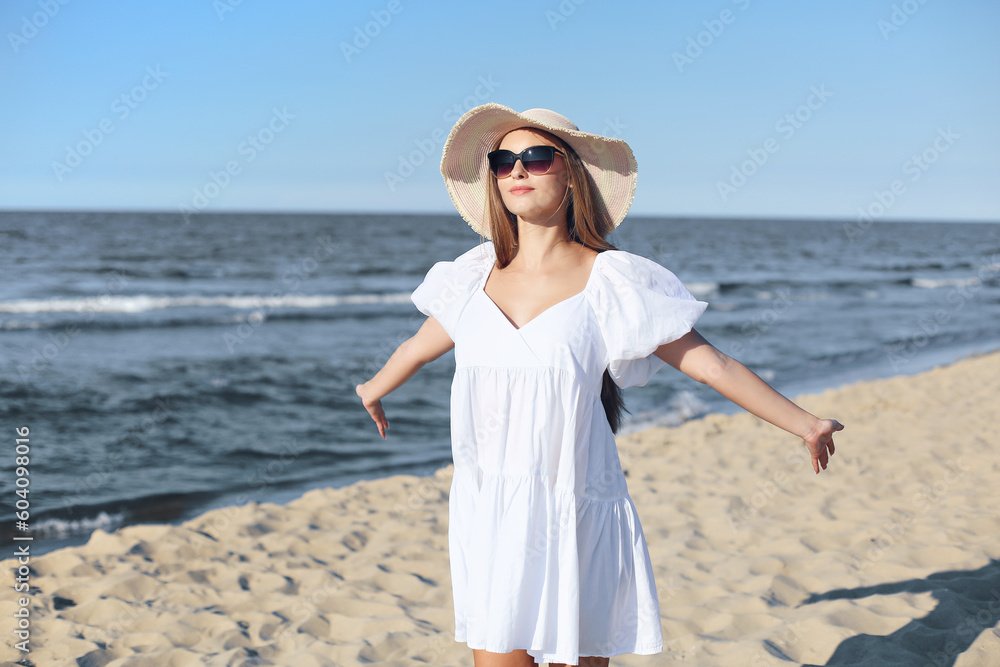 Happy blonde woman is on the ocean beach in a white dress and sunglasses, open arms.