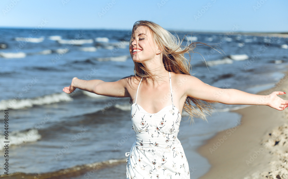 Happy blonde beautiful woman on the ocean beach standing in a white summer dress, raising hands. Happy blonde beautiful woman on the ocean beach standing in a white summer dress, raising hands.
