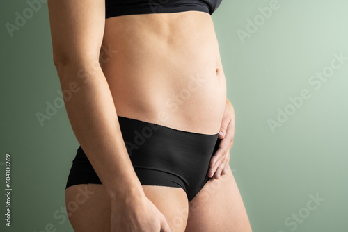 Midsection view of an unrecognizable woman in the first months of pregnancy holding her belly with her left hand. Pregnancy first trimester - week 18. Side view. Mint colored background. Bright shot. © Michael