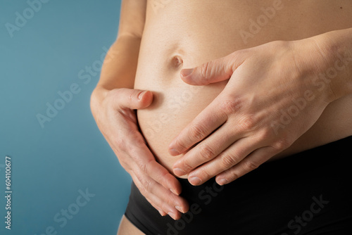 Very close up view of pregnant woman holding her belly gently during first months of pregnancy. Pregnancy first trimester - week 18. Side angle view. Blue background. Bright shot.