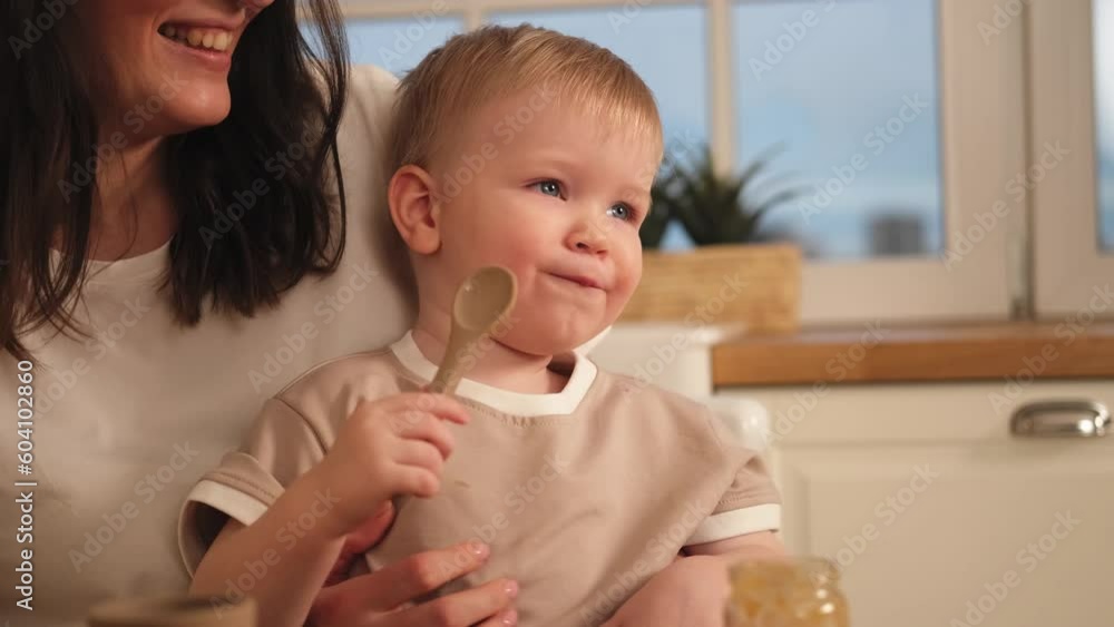Happy family at home. Mother feeding baby in kitchen. Little boy with messy funny face eats healthy food. Child learns eat by himself holding spoon. Woman mom giving food to kid son. Self feeding Happy family at home. Mother feeding baby in kitchen. Little boy with messy funny face eats healthy food. Child learns eat by himself holding spoon. Woman mom giving food to kid son. Self feeding