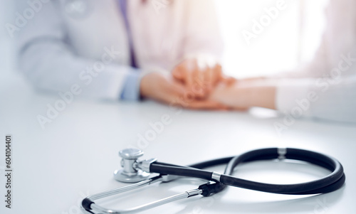 Stethoscope lying on the tablet computer in front of a doctor and patient sitting near each other. Medicine, reassuring hands concept.