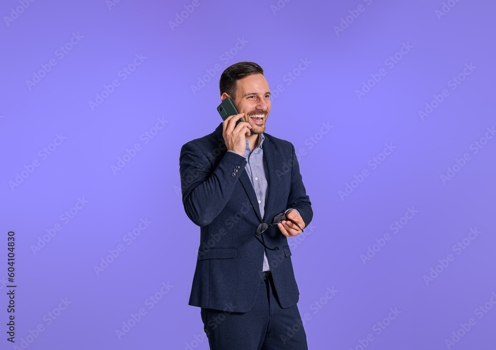 Young handsome executive dressed in elegant suit laughing and talking over mobile phone. Male entrepreneur cheerfully having a business conversation with client while standing Young handsome executive dressed in elegant suit laughing and talking over mobile phone. Male entrepreneur cheerfully having a business conversation with client while standing