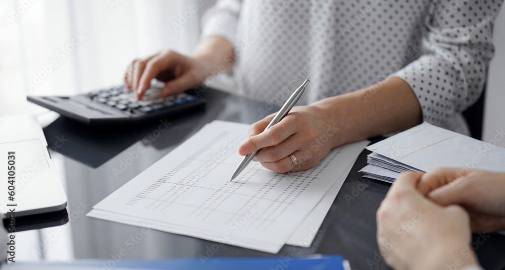 Woman accountant using a calculator and laptop computer while counting taxes for a client. Business audit and finance concepts. Woman accountant using a calculator and laptop computer while counting taxes for a client. Business audit and finance concepts.