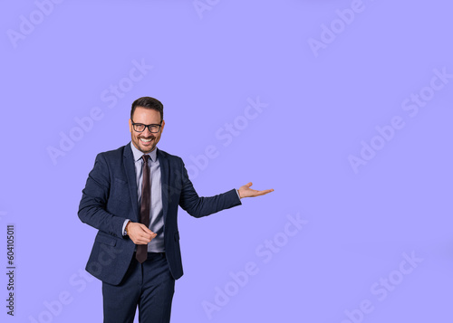 Portrait of smiling male professional executive showing copy space for business marketing. Young salesman dressed in elegant suit advertising something while standing isolated against blue background