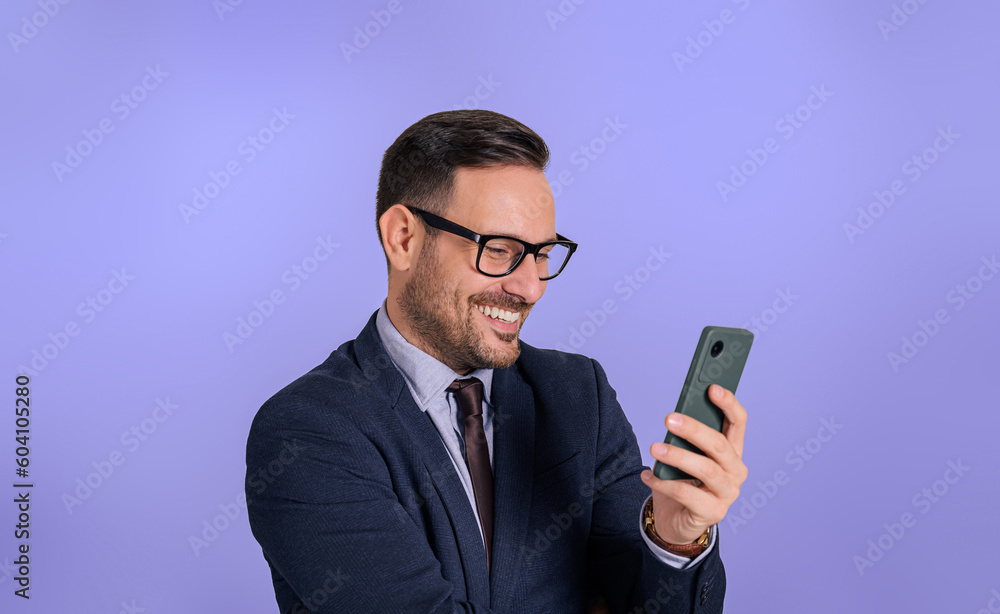 Portrait of smiling young business executive text messaging over smart phone. Charming happy male manager dressed in elegant formals chatting over cellphone against isolated blue background Portrait of smiling young business executive text messaging over smart phone. Charming happy male manager dressed in elegant formals chatting over cellphone against isolated blue background