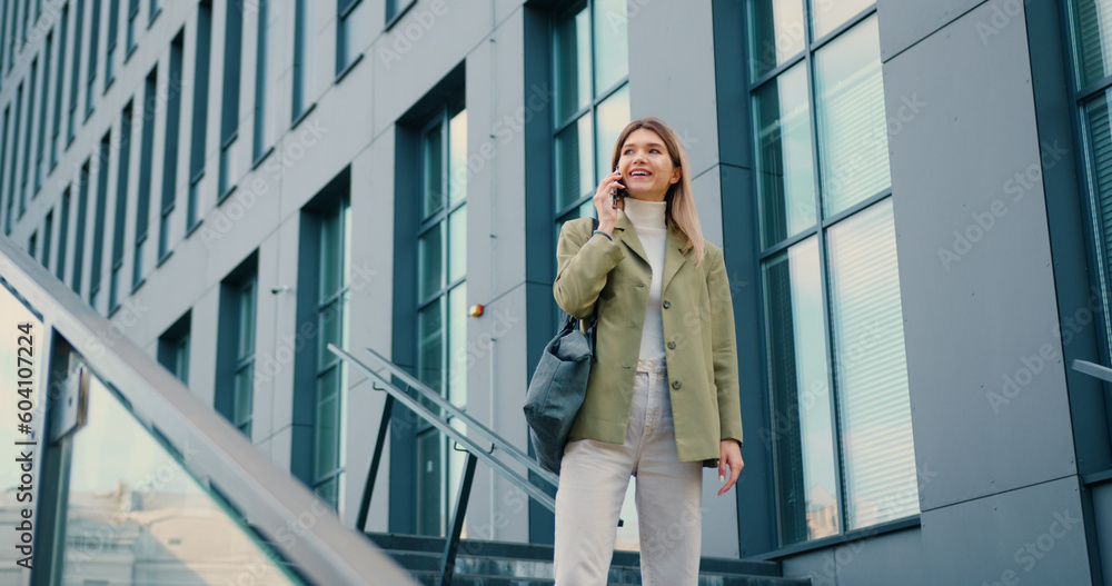 Pretty young smiling woman looking on watch while talking on smartphone during walking in urban city outdoors Pretty young smiling woman looking on watch while talking on smartphone during walking in urban city outdoors