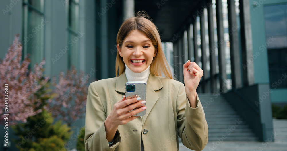 Excited female user customer standing in urban street using smartphone, get amazing sale offer winning online bid, feel ecstatic reading great online news at outside Excited female user customer standing in urban street using smartphone, get amazing sale offer winning online bid, feel ecstatic reading great online news at outside