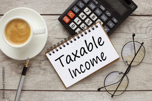 Taxable Income top view of notepad with text and calculator. cup of coffee on the work table