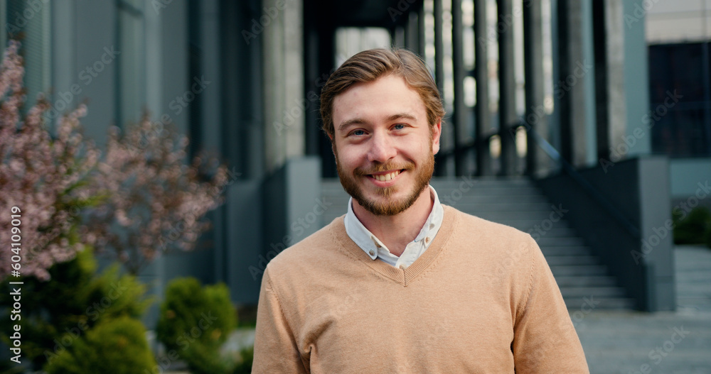 Close-up portrait of handsome success man, looking up at camera, smiling at office building background. Outdoors Close-up portrait of handsome success man, looking up at camera, smiling at office building background. Outdoors