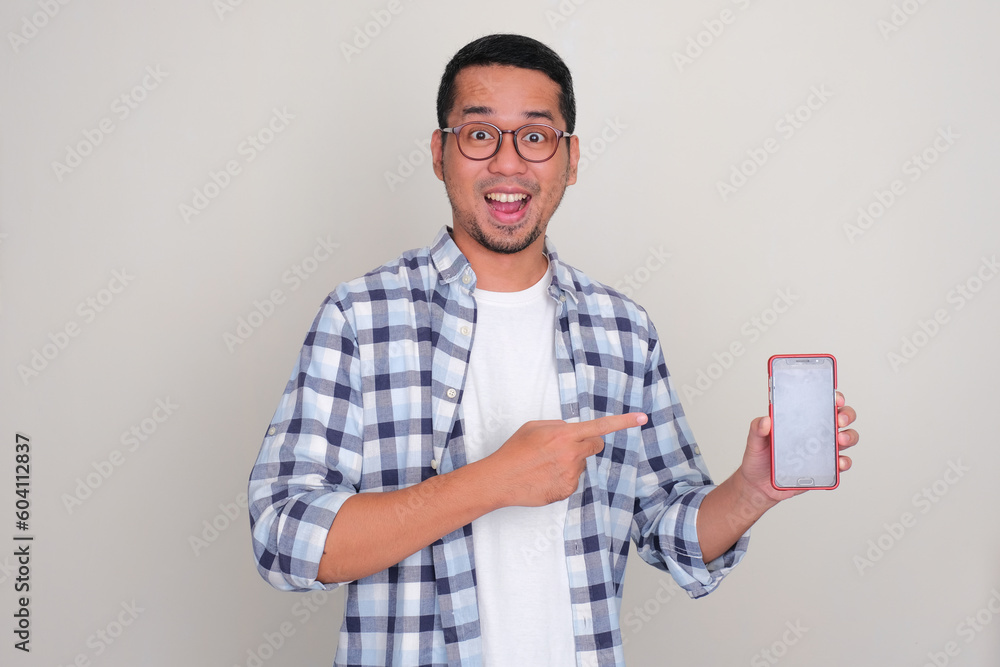 Adult Asian man showing blank mobile phone screen and pointing at it with excited expression Adult Asian man showing blank mobile phone screen and pointing at it with excited expression