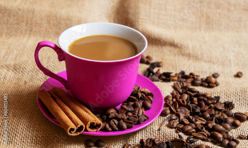 Red cup and saucer with coffee and coffee beans on a brown rag background.